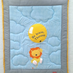 May include: A blue and yellow baby quilt with a lion holding a yellow balloon that says "Be brave, Theresa". The quilt has a gray border with white polka dots.