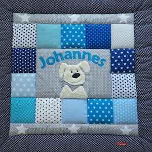 Könnte beinhalten: Eine blaue und weiße Patchwork-Baby-Spielmatte mit einem Plüsch-Hundeapplique und dem Namen "Johannes" in der Mitte gestickt.