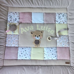 Könnte beinhalten: Eine braune und beige Baby-Spielmatte mit Patchwork-Design. Die Matte zeigt einen braunen Teddybär mit einem gelb gestickten Namen "Ava Luisa".
