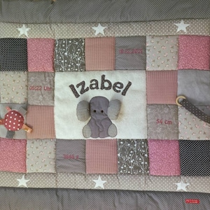 Könnte beinhalten: Eine rosa und graue Baby-Spielmatte mit Patchwork-Design. Die Matte zeigt einen grauen Elefanten mit dem Namen "Izabel", der darüber gestickt ist. Die Matte enthält auch ein kleines, rot-weiß gepunktetes Spielzeug.