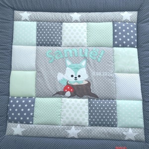 Może przedstawiać: Jasnoniebieska i szara kołderka dla niemowląt z aplikacją lisa i wyhaftowanym imieniem "Samuel!" Kołderka ma patchworkowy wzór z różnymi wzorami gwiazd, kropek i kształtów geometrycznych. Data "11.08.2020" jest również wyszyta na kołderce.