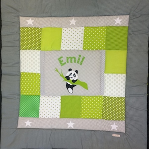 Peut inclure: Une couverture pour bébé en patchwork avec un motif de panda. La couverture a une bordure grise et un panneau central avec le nom "Emil" et une illustration de panda. Le patchwork comprend des carrés verts et blancs à pois et des carrés verts unis.