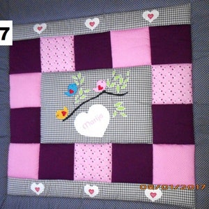Può includere: Una copertina per neonati in patchwork rosa e viola con un cuore bianco al centro che dice "Marja". La copertina ha un motivo a quadri ed è decorata con uccelli e foglie ricamate.