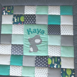 Può includere: Una trapunta per neonati in patchwork verde e grigio con un topo e il nome "Kaya" ricamato.