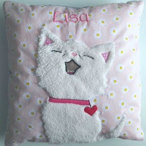 Könnte beinhalten: Ein rosa Kissen mit einem weißen Gänseblümchenmuster. Das Kissen hat eine weiße, flauschige Katze mit einem rosa Halsband und einem roten Herz, das darauf gestickt ist. Der Name "Lisa" ist auf das Kissen gestickt.