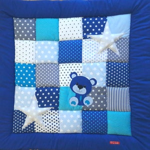 Op de afbeelding: Een blauwe en witte patchwork babydeken met een blauwe teddybeer en witte sterren die erop zijn gestikt.