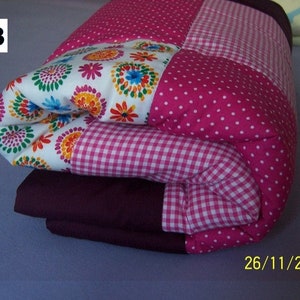 Op de afbeelding: Gevouwen patchworkdeken met verschillende patronen. Het bevat witte stof met kleurrijke bloemmotieven, roze stippen en roze en witte ruitjes. De randen zijn effen donkerpaars. Het nummer "33" staat in de linkerbovenhoek.