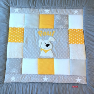 Könnte beinhalten: Eine graue und gelbe Patchwork-Babydecke mit einem weißen Hundeapplique und dem Namen "Paul" bestickt.