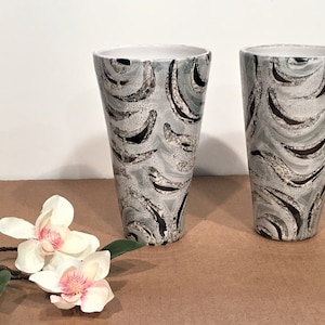 May include: Two ceramic vases with a gray and black abstract pattern. The vases are tall and slender with a flared opening.