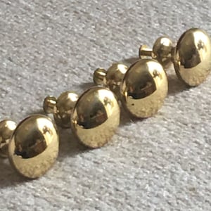 May include: Five gold-toned cabinet knobs with a round, slightly domed shape. Each knob has a small, round stem on the back for attaching to a cabinet door.