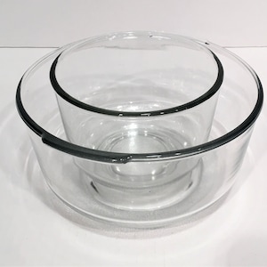 May include: A clear glass serving bowl set. The set includes a large bowl, a smaller bowl, and a lid. The rims of the bowls have a dark gray trim. The bowls are nested together.