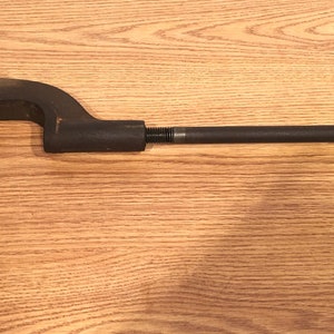 May include: A black pipe cutter with a T-shaped handle. The cutter is made of metal and has a  mechanism for gripping and cutting pipe.