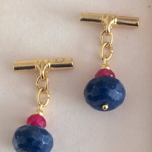 May include: A pair of gold cufflinks, each featuring a blue gemstone and a red gemstone.