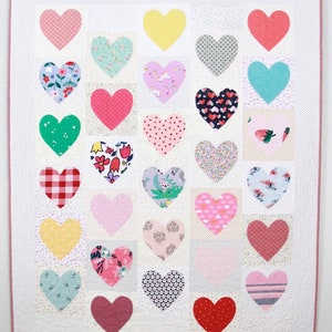 May include: A handmade quilt featuring a grid of colorful heart appliqués on a white background. The hearts are various colors and patterns, including polka dots, floral prints, and stripes. The quilt is bordered with a pink trim and a white dotted pattern.