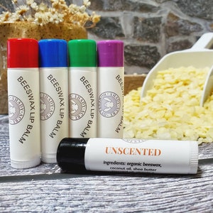 May include: Five different colored lip balms with the label "Beeswax Lip Balm" and a white lip balm with the label "Unscented" and the text "Ingredients: organic beeswax, coconut oil, shea butter".