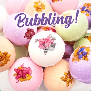 May include: A collection of colorful bath bombs in shades of pink, purple, green, and peach. Each bath bomb is decorated with colorful, decorative sprinkles and the word "Bubbling!" in a purple script font.