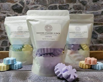 May include: Three clear bags of shower steamers, each with a label. The center bag is filled with purple steamers, labeled "Lavender." The other bags contain pastel-colored steamers. The text "Shower Steamer 10 Pack" is visible on the labels.