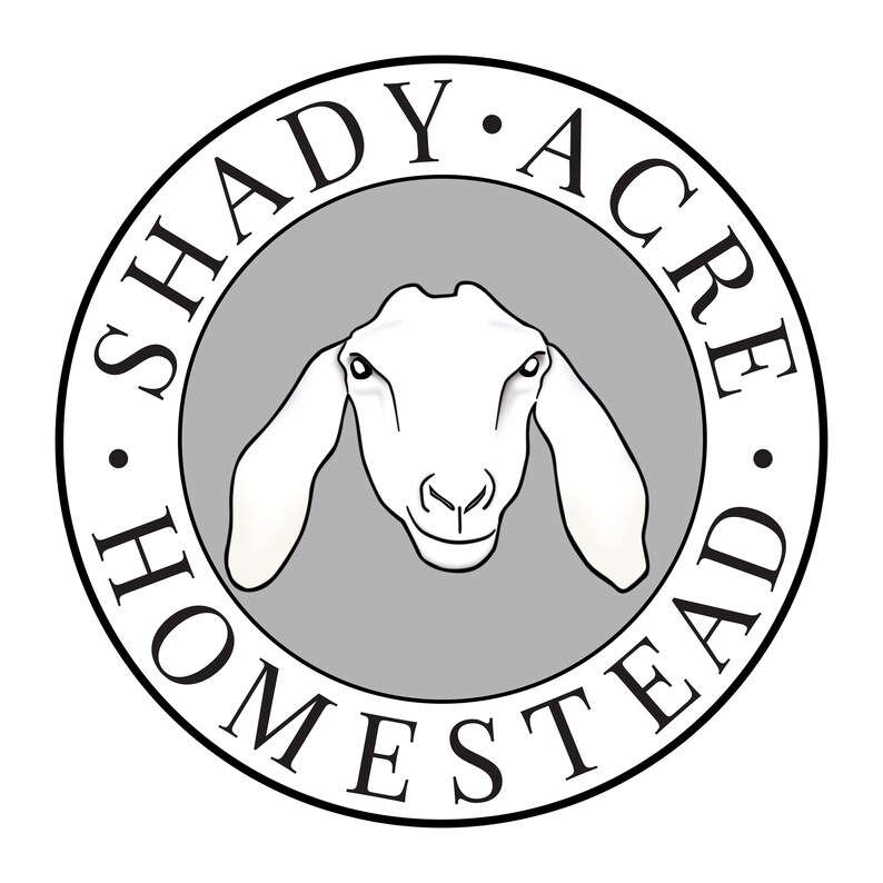 K&ouml;nnte beinhalten: Rundes Logo mit dem Text "SHADY ACRE HOMESTEAD" in schwarzer Schrift. Es zeigt einen wei&szlig;en Ziegenkopf mit langen Ohren in einem grauen Kreis, alles vor wei&szlig;em Hintergrund.