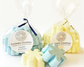 May include: Two bags of shower steamers, one blue and one yellow, with a snowflake design. Each bag is wrapped in clear cellophane and tied with a ribbon. The blue bag is tied with a dark blue ribbon and the yellow bag is tied with a gold ribbon. Each bag has a label that reads "SHADY ACRE HOMESTEAD SHOWER STEAMERS".