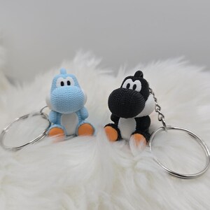 May include: Two character keychains. One is light blue, the other is black and white. Both have orange feet and are attached to silver keyrings. The keychains are sitting on a white, fluffy surface.