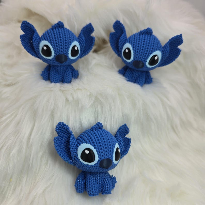 Peut inclure: Trois figurines bleues de Stitch, avec de grandes oreilles et de grands yeux, sont dispos&eacute;es sur une surface blanche et duveteuse. Les figurines sont faites d'un mat&eacute;riau textur&eacute; et ont chacune un petit nez fonc&eacute;.