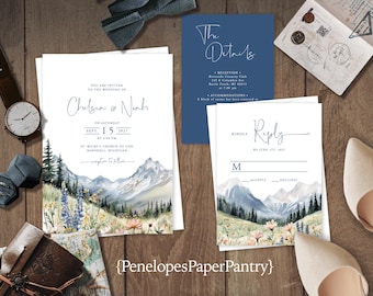 May include: Wedding invitation suite featuring watercolor mountain art. Includes invitation, details card, and reply card. The invitation is addressed to Chelsea & Noah, with the date September 15, 2027. The suite is on a wooden surface.