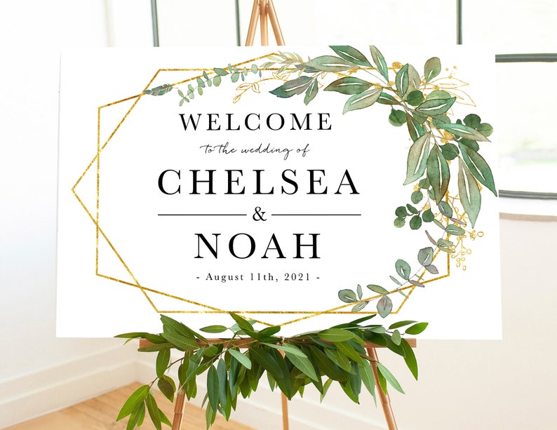 May include: A white welcome sign with a gold geometric frame and green foliage. The text reads "Welcome to the wedding of Chelsea & Noah - August 11th, 2021 -"