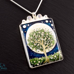 May include: Silver pendant necklace with a rectangular pendant featuring a tree design in front of a full moon. The background is a dark blue with white stars. The pendant has a silver frame and is attached to a silver chain.
