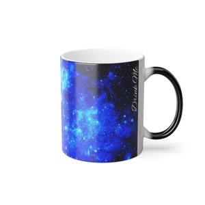 Puede incluir: Una taza mágica en blanco y negro con un diseño de galaxia nebulosa azul. La taza dice "Drink Me" en el lateral.
