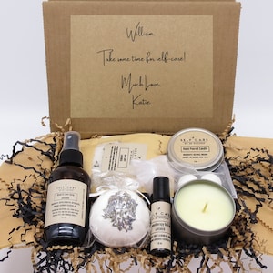 May include: A brown cardboard box filled with self-care items, including a lavender bath bomb, a bottle of body and linen spray, a candle, and a roll-on essential oil. The box is decorated with a handwritten note that says "William, Take some time for self-care! Much Love, Katie."