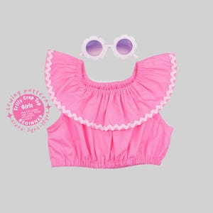 May include: A bright pink crop top with a large ruffled neckline trimmed in white rickrack, paired with white flower-shaped sunglasses. Text on the left reads: Sewing pattern, Frilly Crop Top, Girls, A4/US Letter, A0 Copy Shop, Projector, Layers, BEGINNER, sizes: 3yrs-10yrs.