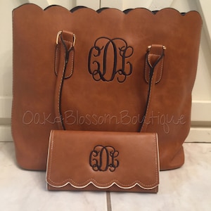 Puede incluir: Un bolso tote de cuero marr&oacute;n y una cartera a juego con bordes festoneados y un dise&ntilde;o de monograma. El monograma es "GDL" en hilo negro.