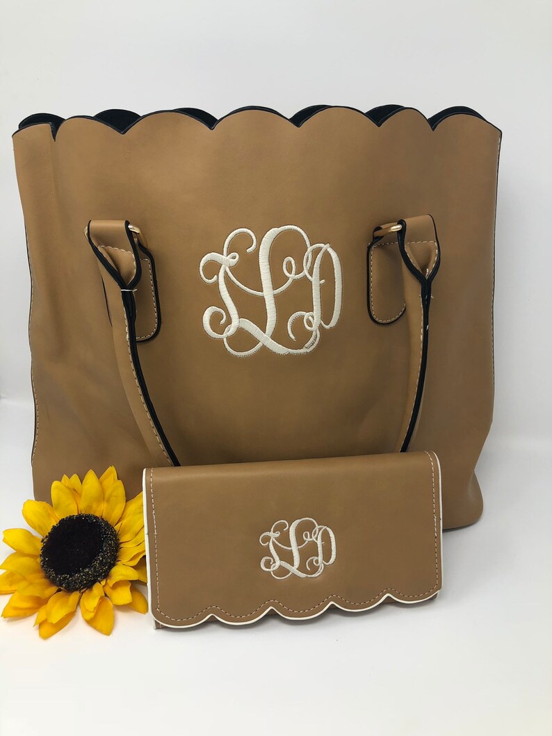 Puede incluir: Un bolso tote de cuero marr&oacute;n con un borde festoneado y ribete negro. El bolso tiene dos asas y una cartera de cuero marr&oacute;n a juego con un borde festoneado y ribete blanco. Tanto el bolso como la cartera tienen un monograma blanco "LLD" bordado en la parte delantera.