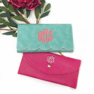 Puede incluir: Dos carteras monogramadas, una turquesa con bordes blancos festoneados y la otra rosa intenso. Ambas carteras presentan el monograma "SMS" en una fuente de letra blanca.