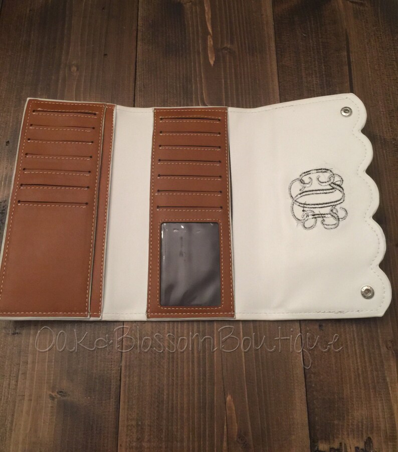 Puede incluir: Cartera de cuero blanco de tres pliegues con interior de cuero marr&oacute;n y borde festoneado. La cartera tiene m&uacute;ltiples ranuras para tarjetas, una ventana de identificaci&oacute;n transparente y una inicial bordada.