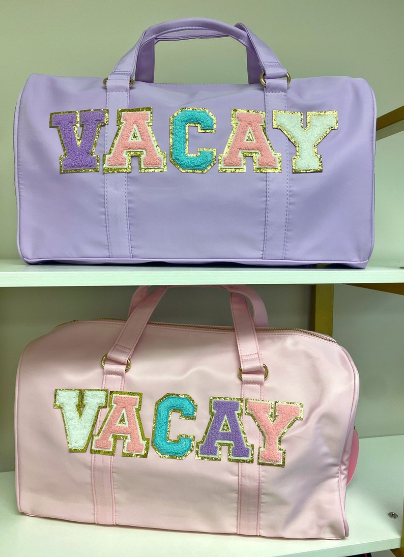 Pu&ograve; includere: Due borsoni da viaggio con la parola "VACAY" scritta in lettere colorate e pelose. La borsa in alto &egrave; lavanda e la borsa in basso &egrave; rosa.