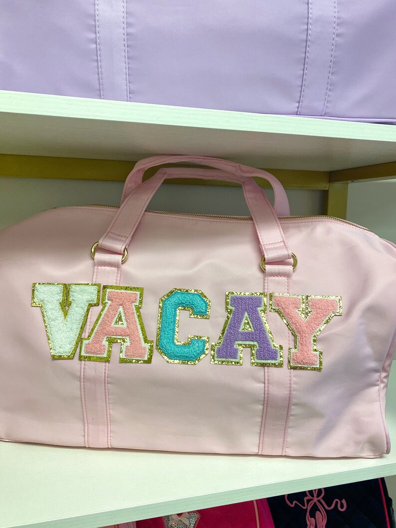 Pu&ograve; includere: Borsa da viaggio rosa con la parola "VACAY" scritta in lettere colorate e scintillanti.