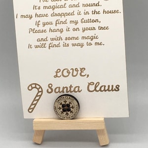 以下が含まれることがあります： 白いカードに金色の文字で「Help I've lost a button. It's magical and round. I may have dropped it in the house. If you find my button, please hang it on your tree and with some magic it will find its way to me. LOVE, Santa Claus」と書かれています。カードには、木製のキャンディーケーンと、雪の結晶のデザインと「Santa Claus Property of the North Pole」という文字が書かれた木製のボタンがあります。