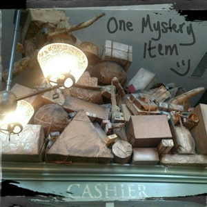 May include: A pile of wrapped packages and boxes with a sign that reads "One Mystery Item" and "CASHIER". Two light fixtures with ornate glass shades hang from the ceiling.