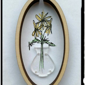 May include: A wooden oval frame with a clear plastic vase and yellow flowers inside. The flowers are drawn in black ink and colored yellow.
