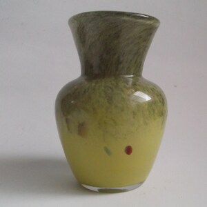 May include: A small, green and yellow glass vase with a mottled finish. The vase has a round body and a narrow neck.