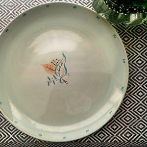 Puede incluir: Un plato de cena de cerámica blanca con un borde azul claro y un delicado diseño floral en tonos marrones, verdes y rosas.