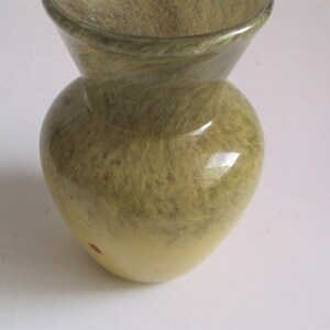 May include: A small, green and yellow glass vase with a swirl pattern. The vase has a wide mouth and a narrow base.