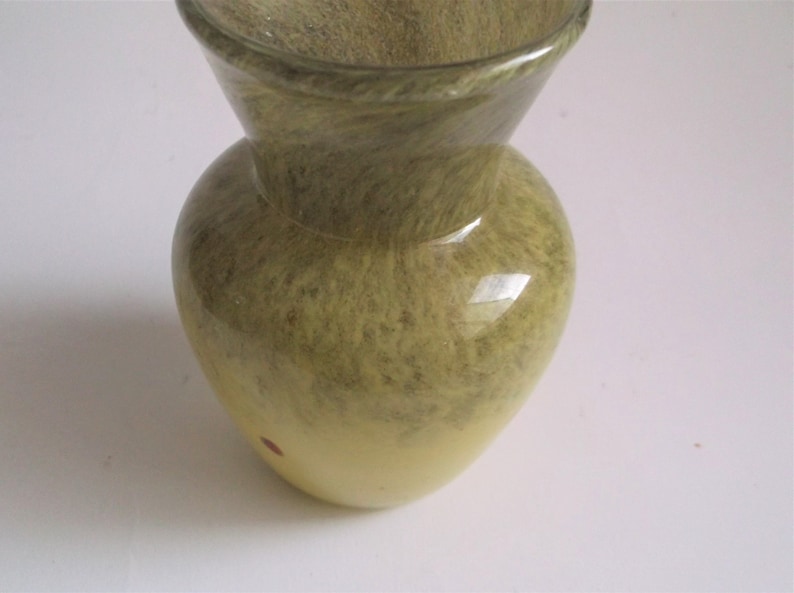 May include: A small, green and yellow glass vase with a swirl pattern. The vase has a wide mouth and a narrow base.