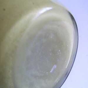May include: Close-up of the bottom of a clear glass jar with a light yellow liquid inside.