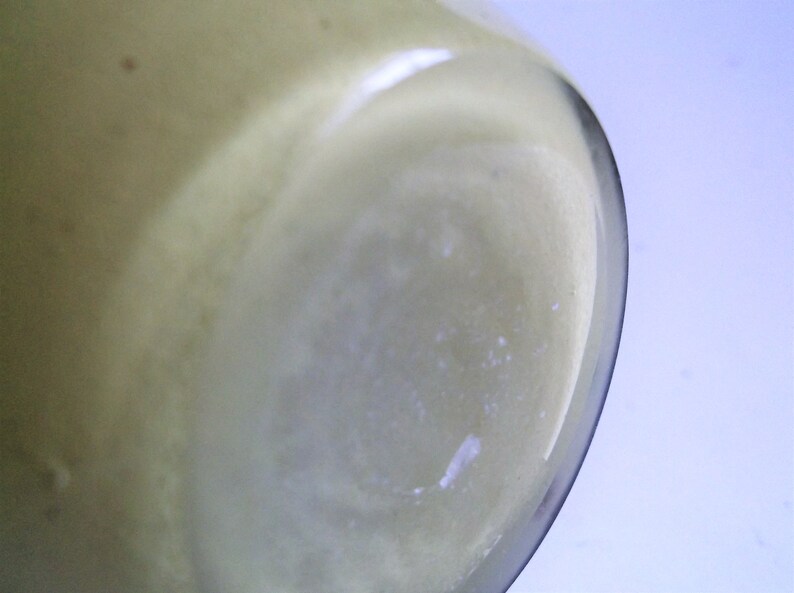 May include: Close-up of the bottom of a clear glass jar with a light yellow liquid inside.