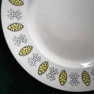May include: White ceramic plate with a black and yellow floral design around the edge.