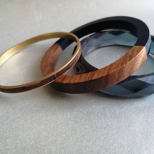 Puede incluir: Tres pulseras apiladas una encima de la otra. La pulsera superior es negra con una incrustación de madera. La pulsera del medio es de madera con una incrustación dorada. La pulsera inferior es de vidrio azul oscuro facetado.