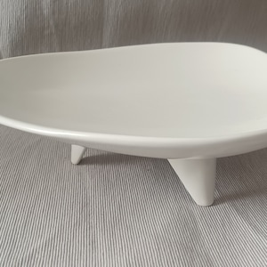 Puede incluir: Plato de servir de cerámica blanca con una forma orgánica única y tres patas. El plato es perfecto para exhibir fruta, aperitivos u otros artículos pequeños.