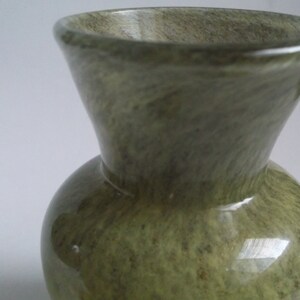 May include: A green glazed ceramic vase with a marbled pattern. The vase has a wide mouth and a rounded body.